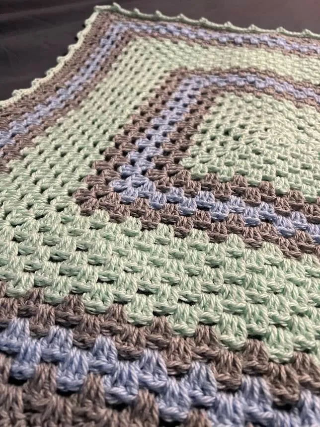 A granny-square baby blanket in sage, lavender and grey
