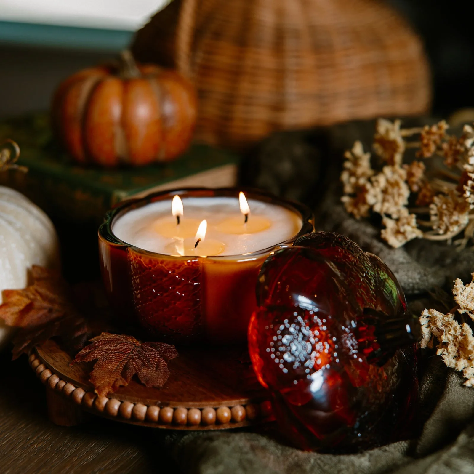 A three-wick candle in an amber glass pumpkin among autumn decor