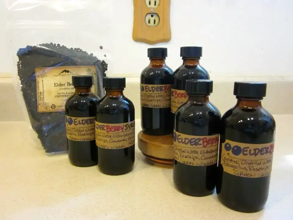 Bottles of elderberry syrup beside a bag of dried elderberries