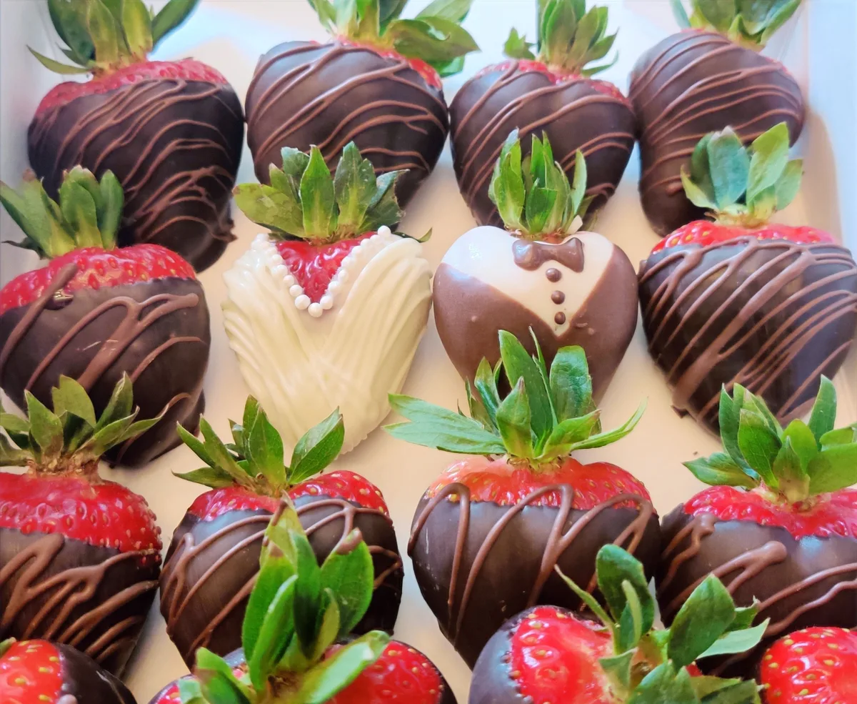 A tray of chocolate-covered strawberries, some dressed as a bride and groom