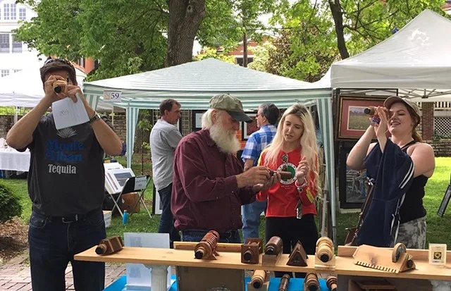 Visitors looking through kaleidoscopes at an outdoor art show booth