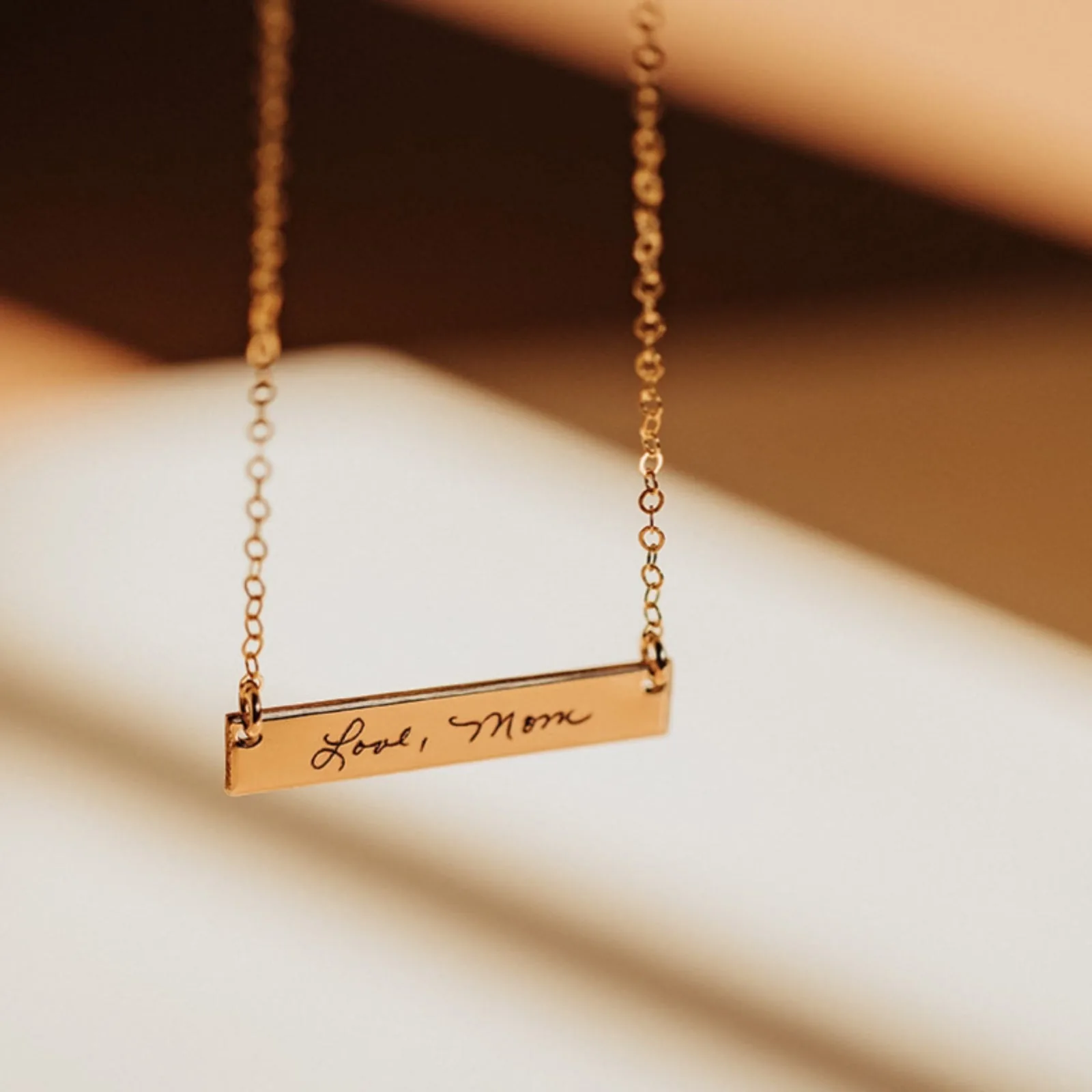 Gold bar necklace engraved in handwriting with "Love, Mom"