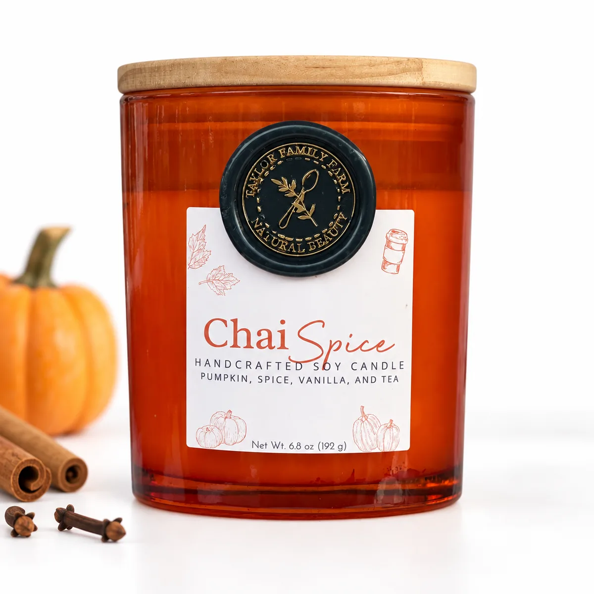 Chai Spice soy candle in orange glass with a small pumpkin and cinnamon sticks