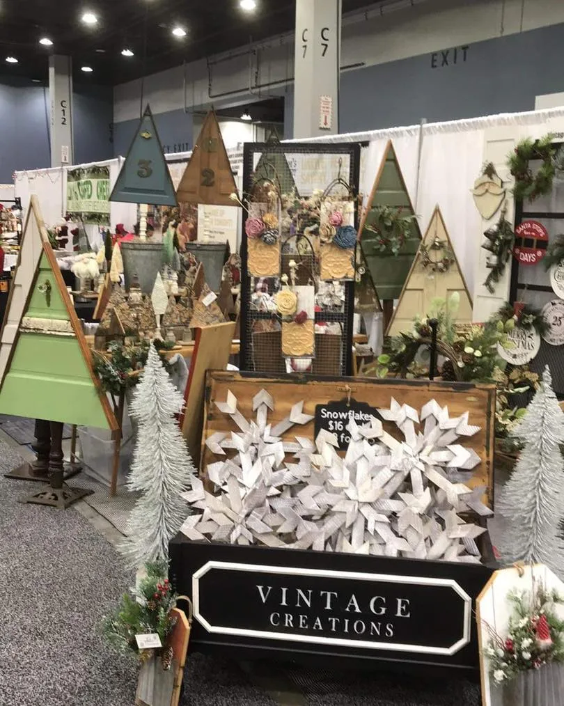 The Vintage Creations holiday booth: wooden trees, wreaths and a crate of white wooden snowflakes